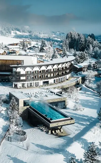 Building with pool in the snow, surrounded by trees and winter landscape.