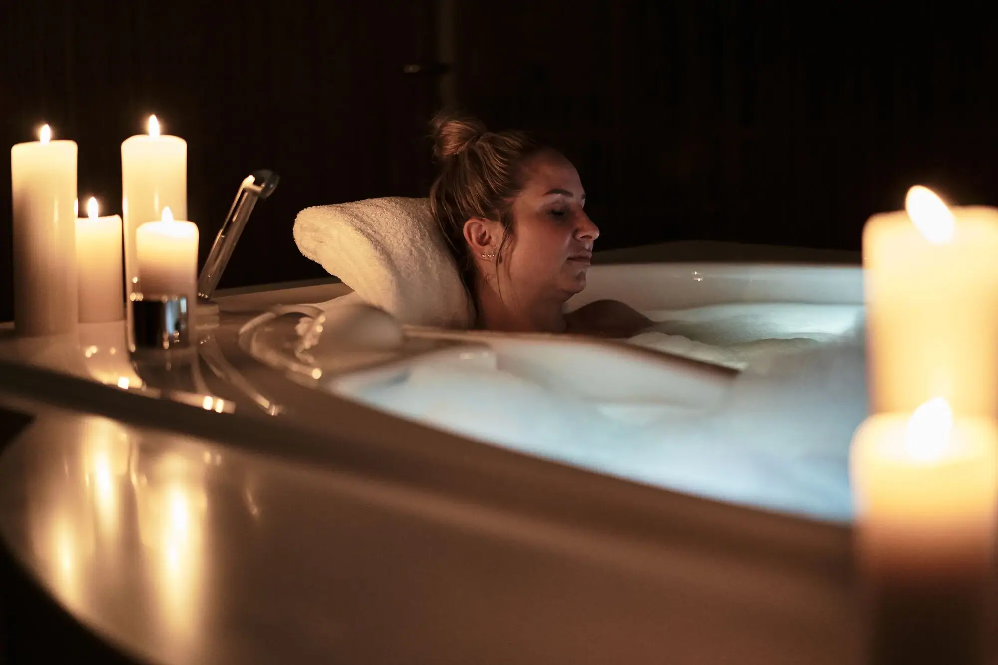 SPA Suites A woman relaxing in a hot tub indoors with candles around.