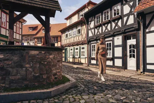 Eine Frau geht auf einer Kopfsteinpflasterstraße, im Hintergrund sind Gebäude zu sehen.