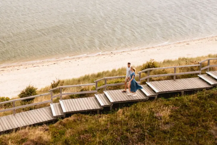 A couple walks along a wooden path through the dunes by the sea. 