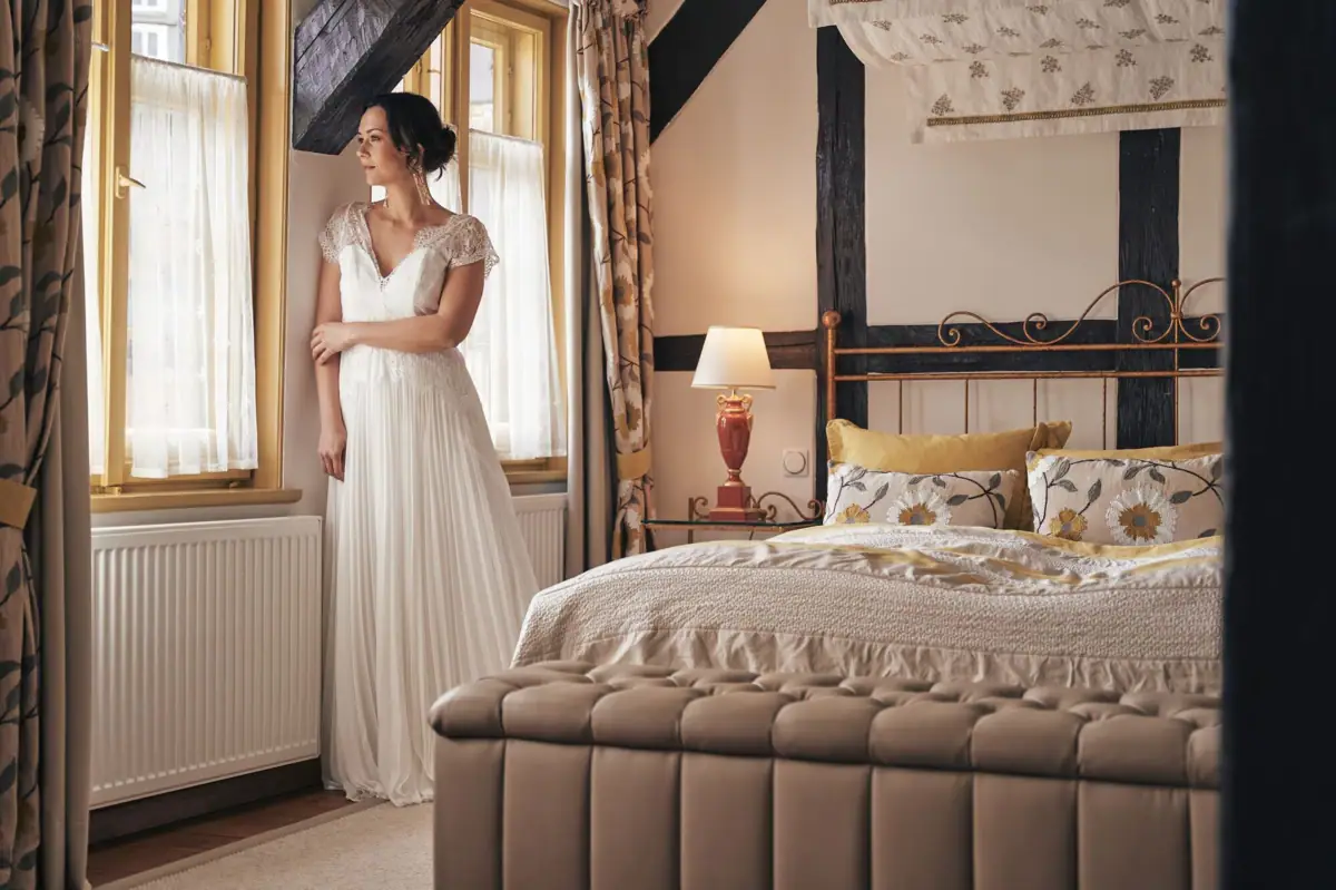 Eine Frau in einem weißen Kleid steht in einem Schlafzimmer.