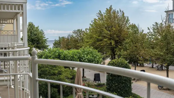 Balcony with a view of a promenade with trees and the sea in the background.