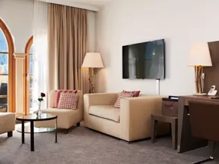 A seating area with three armchairs and a coffee table with a vase containing a red rose. A floor lamp and a beige curtain can be seen behind the armchairs.