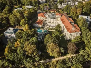 Large building surrounded by lush trees in a residential area.