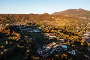 An aerial view of a landscape with trees and buildings, with mountains and the sky in the background.