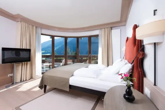 Interior view of a hotel room with a bed and a television with a view of a mountain backdrop.