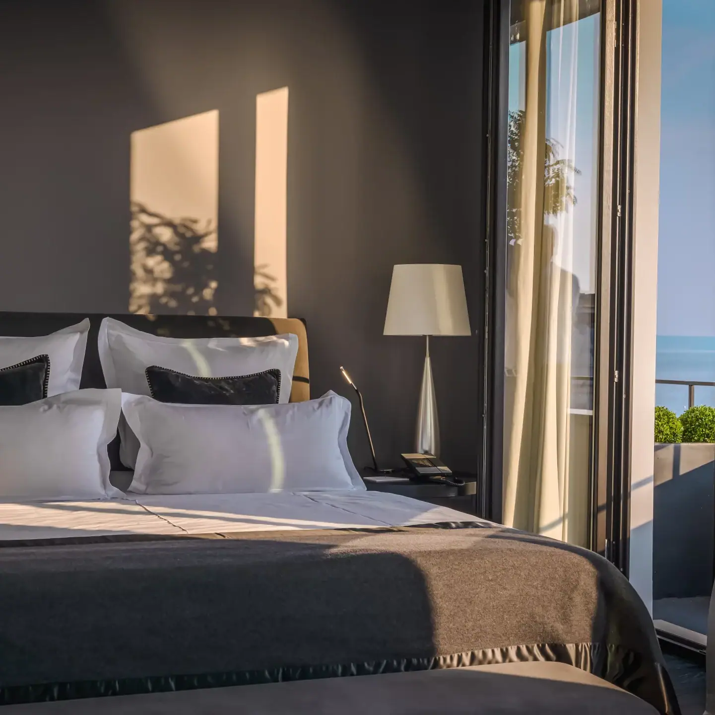 A neatly made bed with pillows and a lamp in a softly lit room.