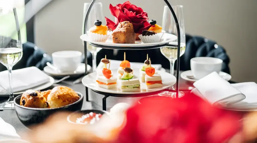 A dining table with an etagere of small snacks and pastries, next to which coffee cups, champagne glasses and plates are spread out. 