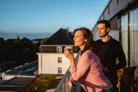 A man and woman standing on a balcony enjoying the morning sun. 