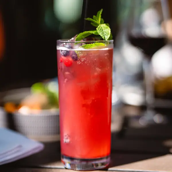 A glass of red drink with mint leaves and a straw.