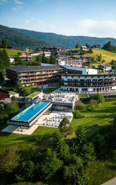 A building with an infinity pool in the middle of a mountain village, surrounded by trees and green spaces.