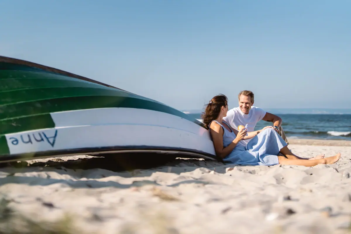 Couple on the beach A man and a woman are sitting on the beach next to a boat.