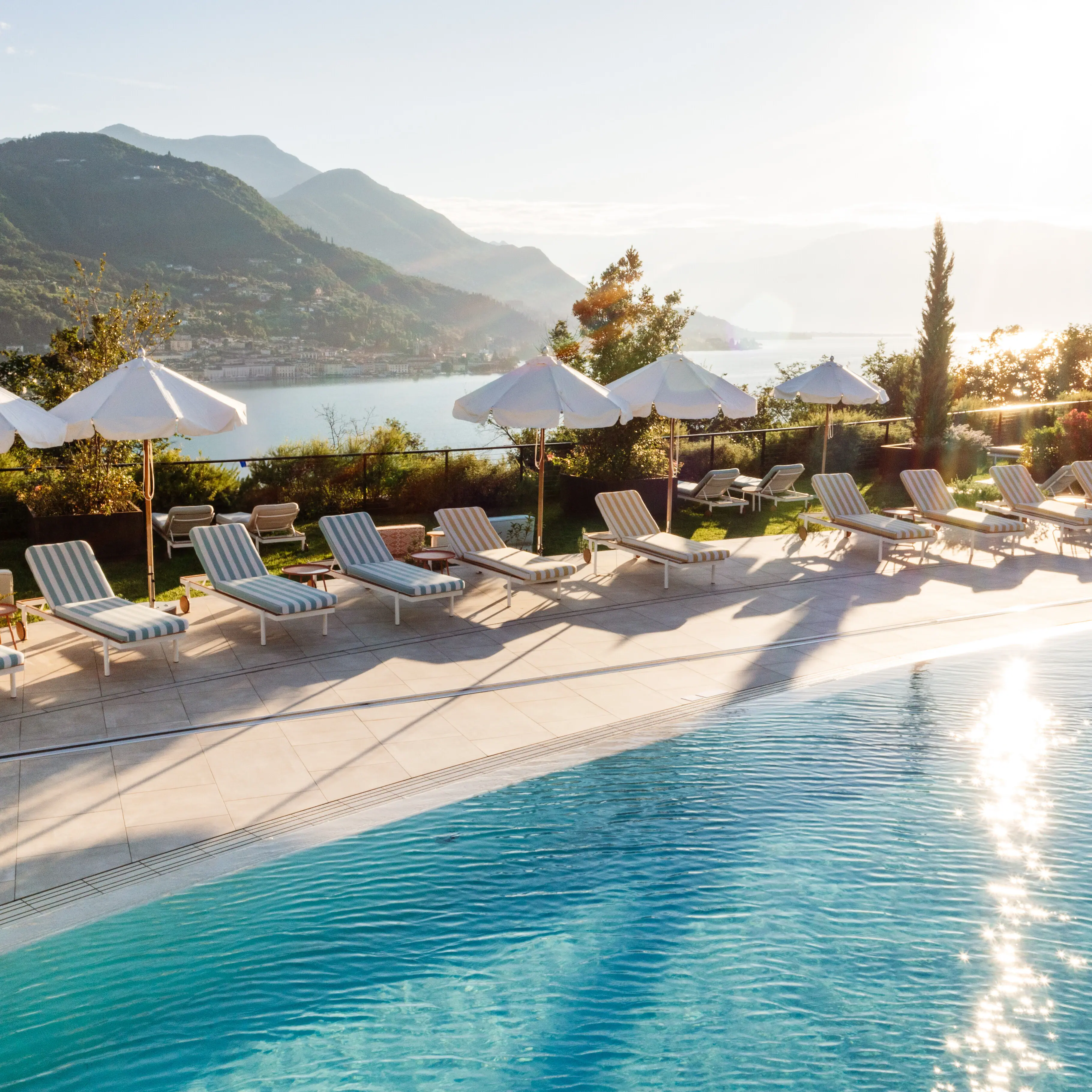 Ein Pool mit Liegestühlen und Sonnenschirmen an einem Gewässer.