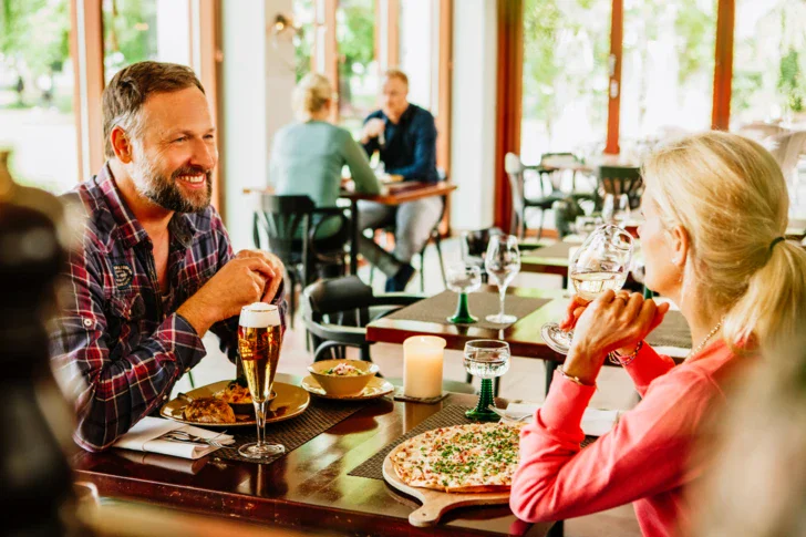 A man and woman sitting at a table enjoying a meal and drinks in a restaurant.