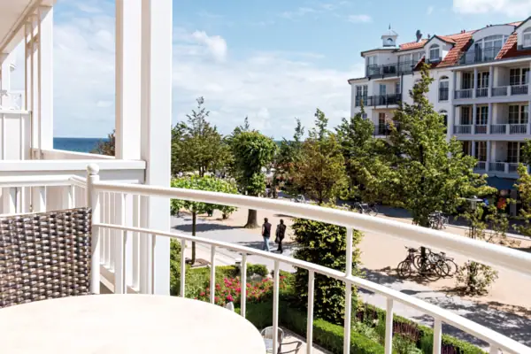 A balcony with a white railing overlooking a street with trees and people walking.