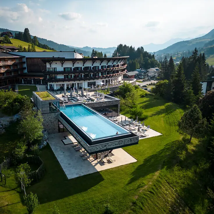Ein Outdoor Infinity Pool in einem Hotel, umgeben von Bäumen und einem klaren Himmel.