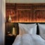 A close-up of a hotel bed with white bed linen standing in front of a wall with historic wooden panels. 