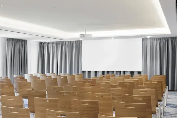 Event room with a projector and screen. A meeting room at A-ROSA Tegernsee with rows of chairs, a projector and a screen.