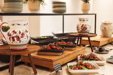 Trays of food on a table with bowls and vases indoors.
