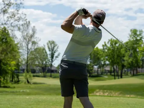 A man swings a golf club on a golf course.