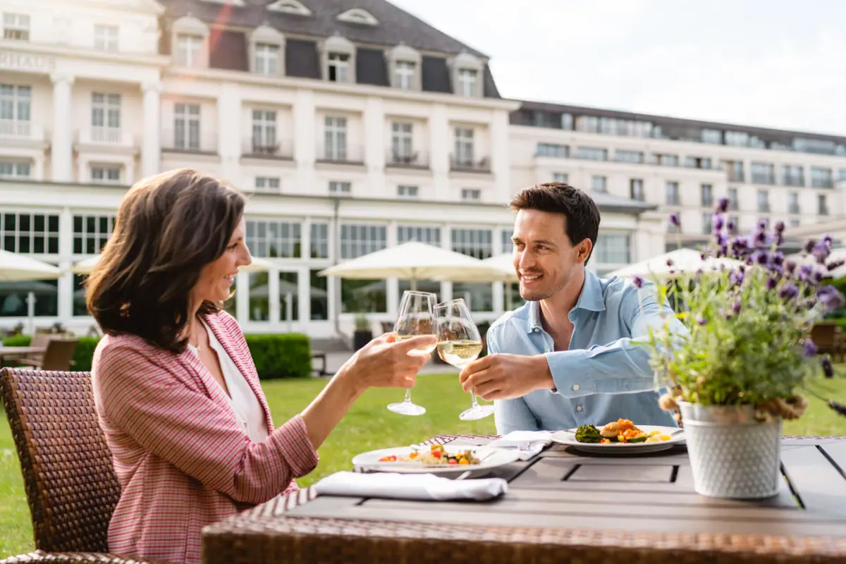 Ein Mann und eine Frau stoßen mit Weingläsern an einem Tisch im Freien an.