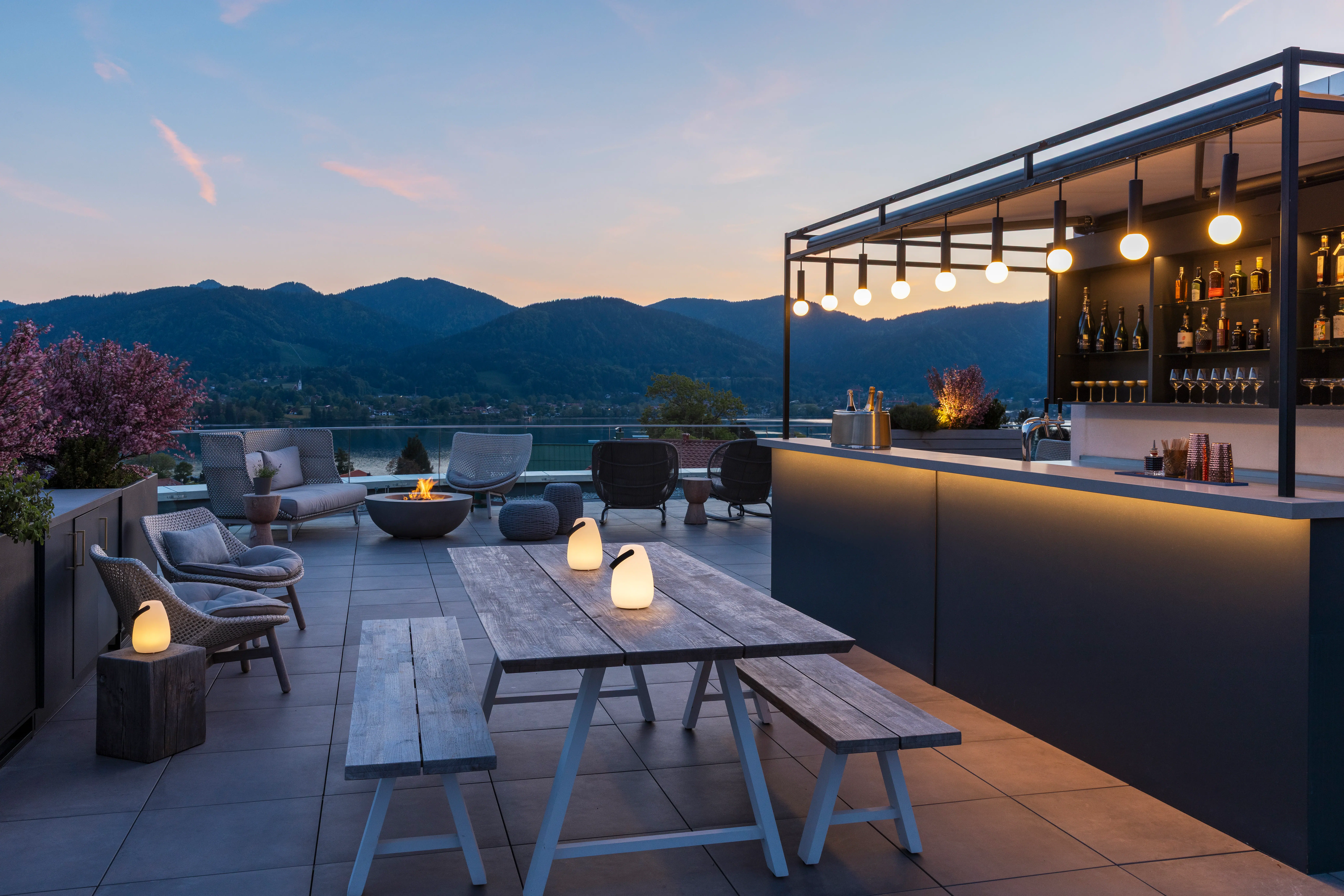 A terrace with a table and chairs, a bar in the background, and a view of a lake.