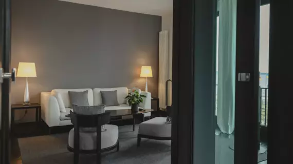 A living area photographed through a glass door in gray tones with a sofa and armchairs with lamps that provide warm light. 