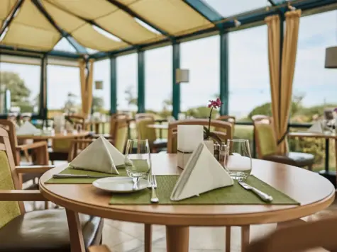 Elegantly laid table in a restaurant conservatory with tablecloth and crockery.