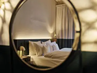 A round mirror was photographed in whose reflection a hotel bed with white bed linen can be seen.