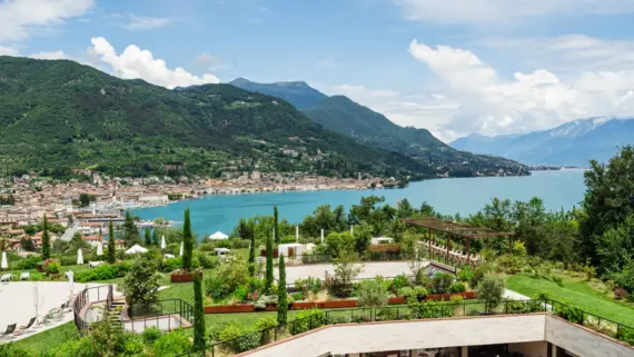 Garden area beside a lake surrounded by trees under a cloudy sky with mountains in the background