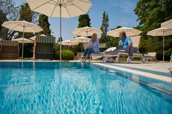 A man and woman relaxing on lounge chairs by a swimming pool in a resort setting.