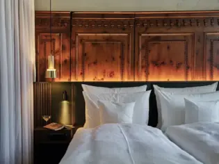 A bed with white pillows and a lamp on a bedside table.