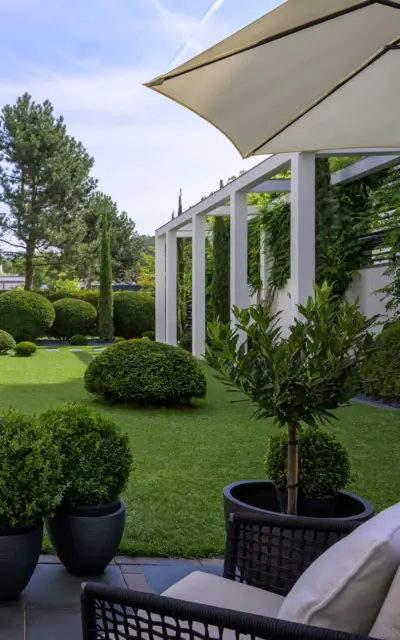 Patio with chairs, tables, and potted plants under a shaded area.