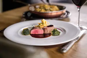 A plate with artfully arranged food on a table, next to it a wine glass.