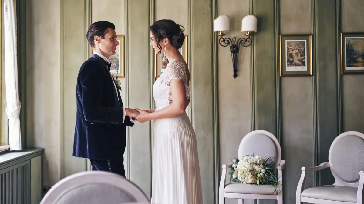 Ein Mann und eine Frau in Hochzeitskleidung halten sich an den Händen.