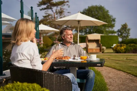 A man and a woman are sitting at a laid breakfast table outside.