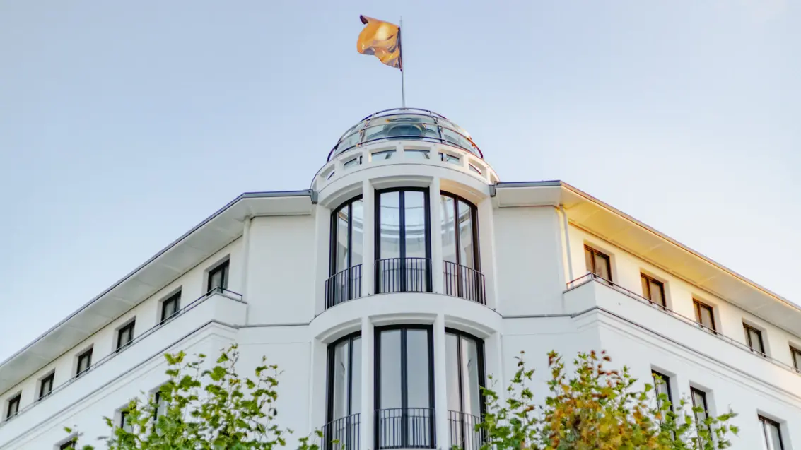 A flag on a glass dome on a white building is illuminated by the sun and blows in the wind.