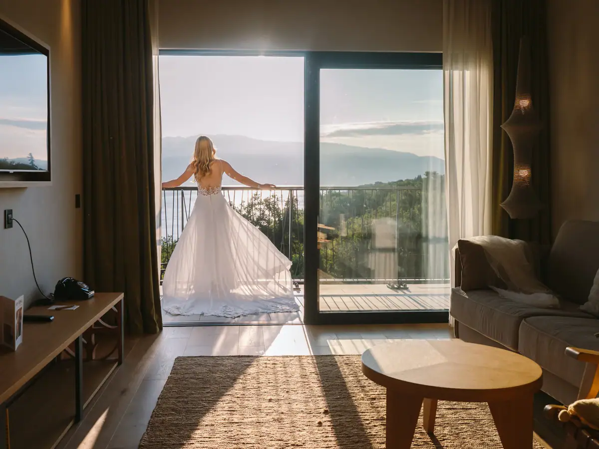 Der große Auftritt Braut öffnet die Balkontüren ihrer Suite und blickt im Hochzeitskleid auf den Gardasee.