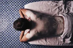 A person is lying on a towel, wrapped in a white body wrap.