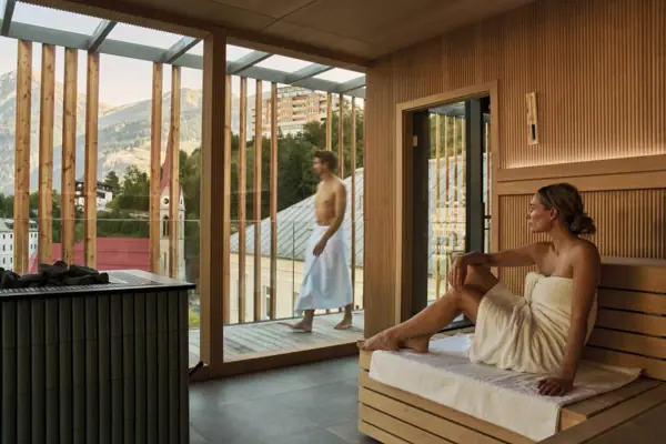 A woman sits in a sauna with a man in a white bathrobe.