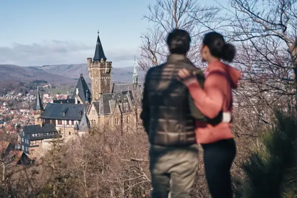 Ein Mann und eine Frau stehen auf einem Hügel und blicken auf ein Schloss.