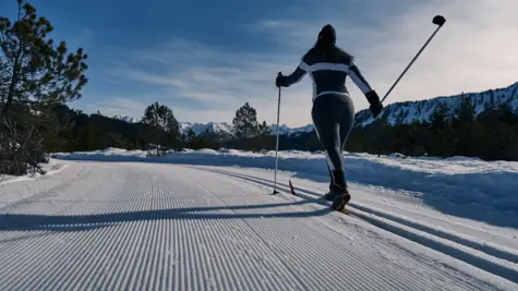 Skier gliding down a snowy road surrounded by trees.