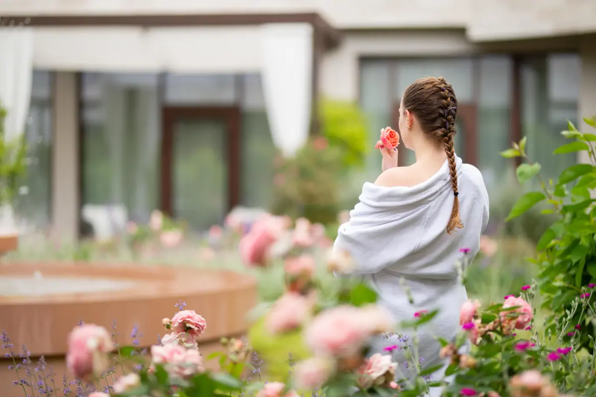 A woman in a bathrobe smelling a flower.