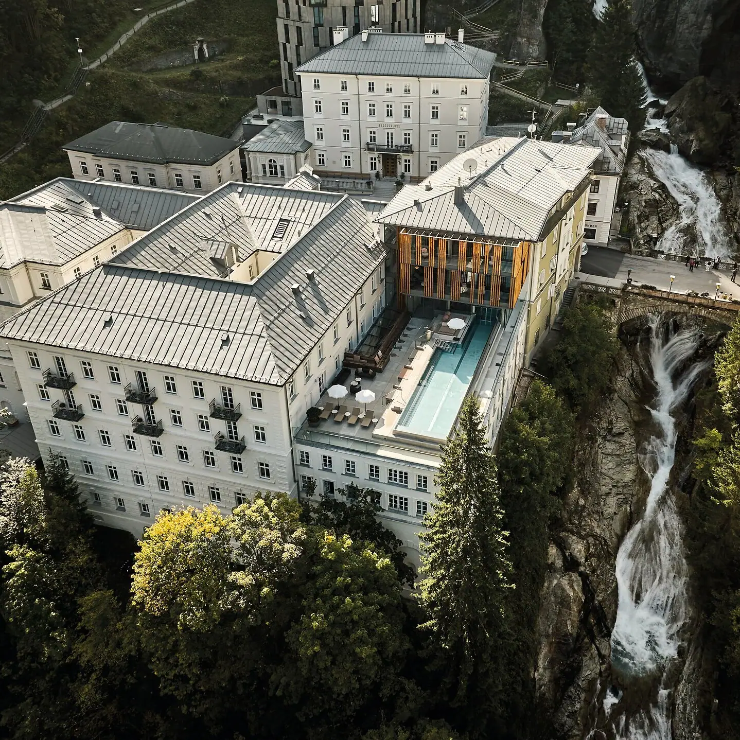 A building with a pool and an outdoor waterfall, surrounded by trees.