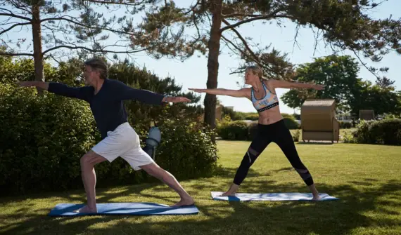 Man and woman doing yoga on a meadow.