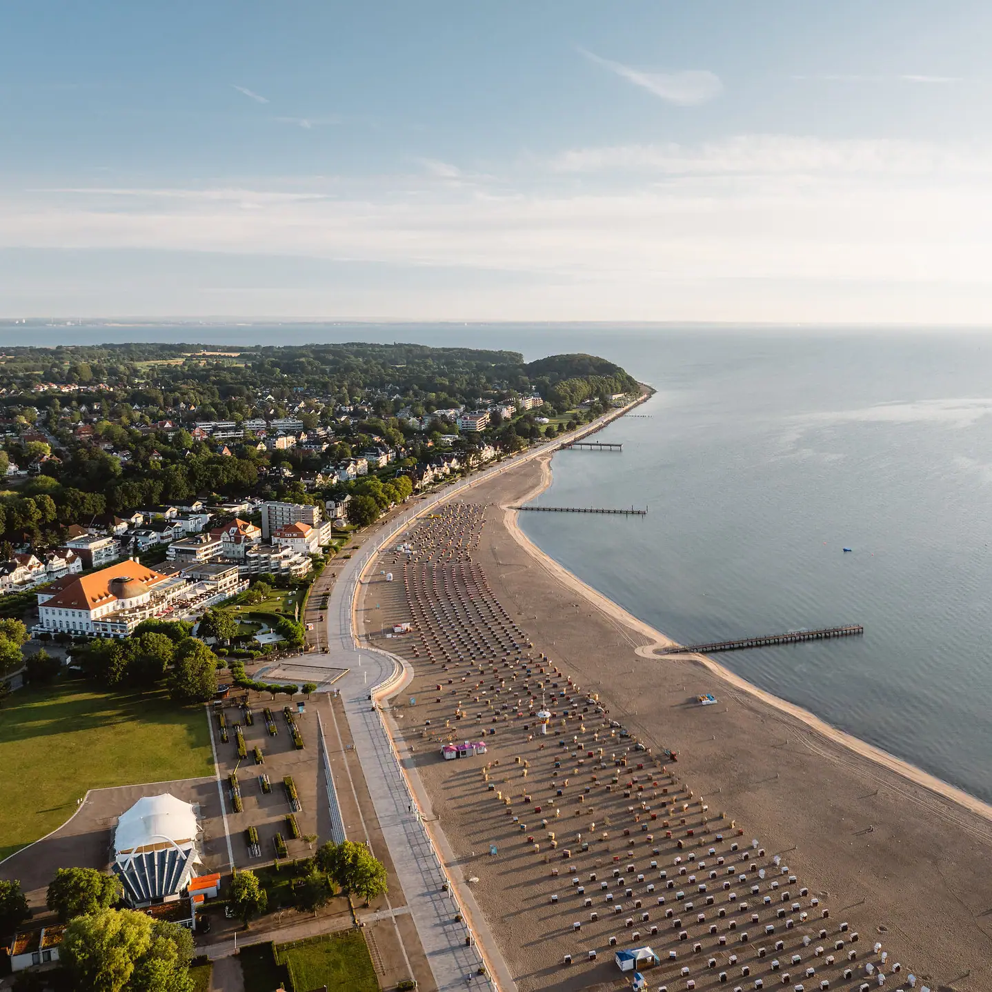Strand mit vielen Sonnenschirmen und Gebäuden am Wasser.