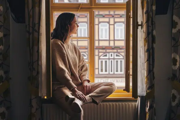 Eine Frau sitzt auf einer Fensterbank und blickt aus dem Fenster.