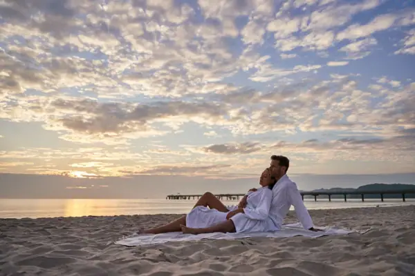 A man and woman sitting on a beach with a cloudy sky.