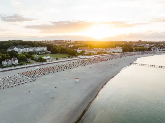 An aerial view of a long beach by the water and buildings behind it in the morning dew at sunrise.