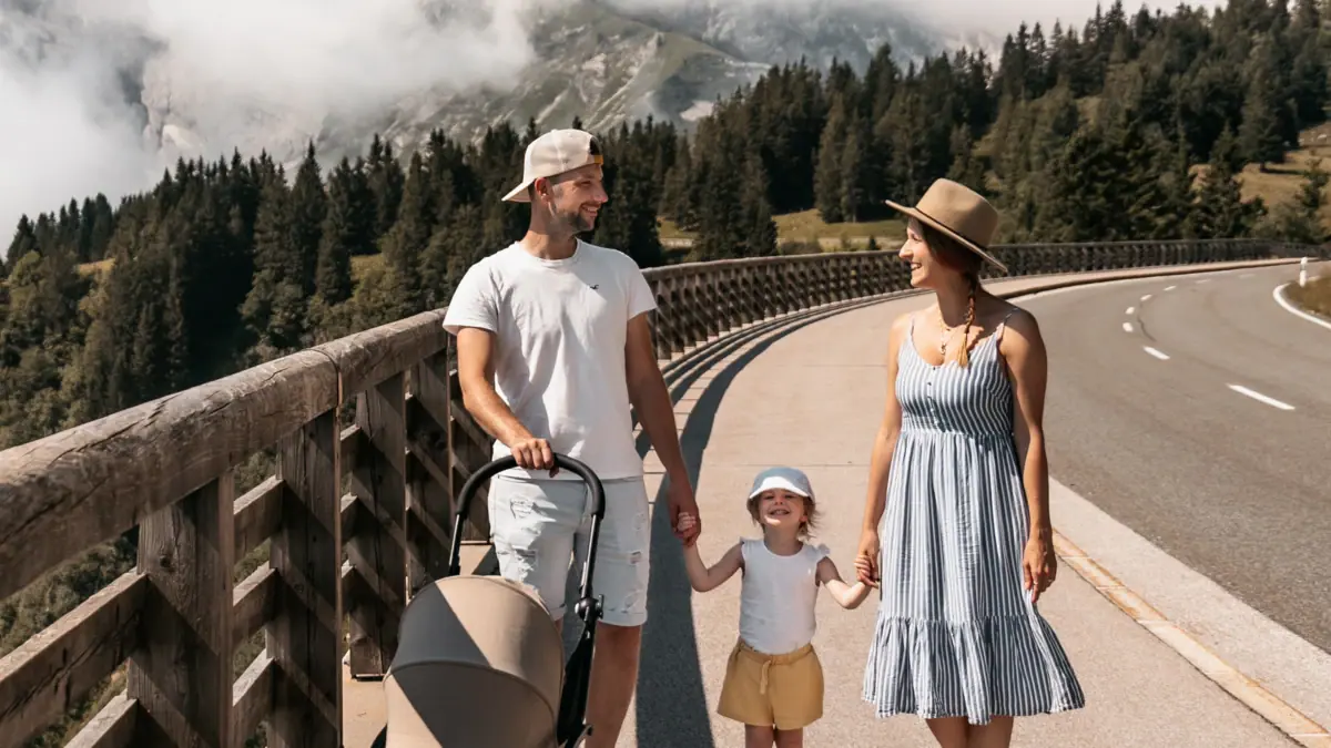 A family is walking across a bridge with a pram; a mountain can be seen in the background.